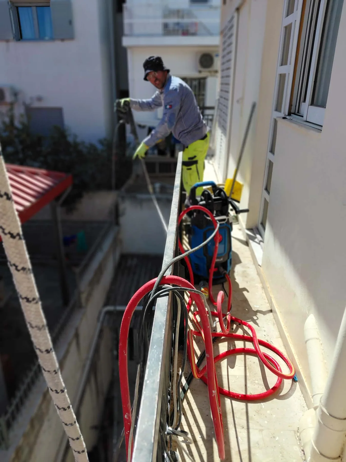 Τεχνίτης σε μπαλκόνι με εξοπλισμό προετοιμασίας για εξωτερικές εργασίες.